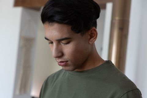 Contemplative african american man looking down in minimal interior wearing olive tee