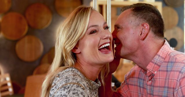 A middle-aged Caucasian couple shares a joyful moment, laughing together with a background of wooden barrels, with copy space. Their happiness and closeness suggest a celebration or a romantic outing at a winery or brewery.