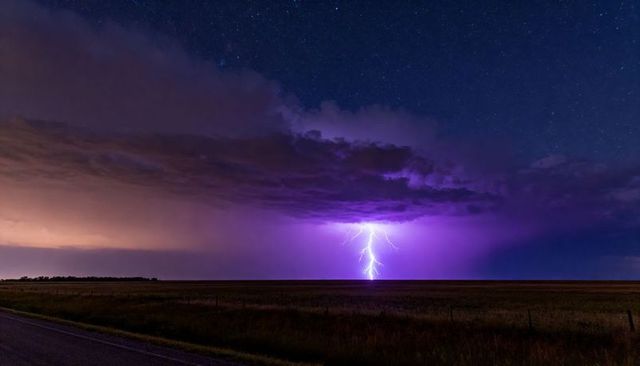 Violet forked lightning striking prairie night with starry sky and rural road