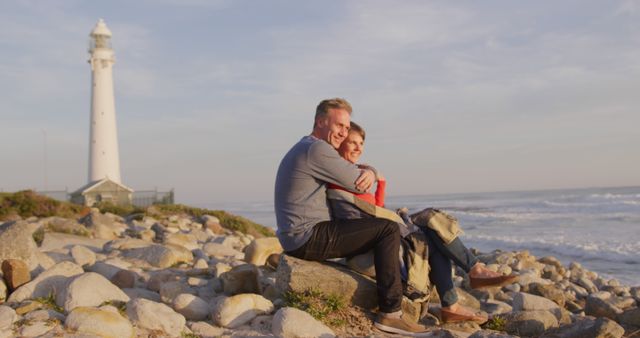 Happy senior caucasian couple sitting on rocky beach embracing in the sun, copy space. Togetherness, relationship, romance, retirement, vacations, wellbeing and active senior lifestyle, unaltered.