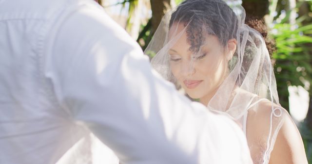 This image captures a close-up of a bride with a veil over her head during an outdoor wedding ceremony. Her serene expression conveys a sense of joy and anticipation. This image is ideal for use in wedding magazines, websites, blogs, or any promotional materials aimed at highlighting wedding-related content. It evokes feelings of romance, celebration, and the beauty of marriage.