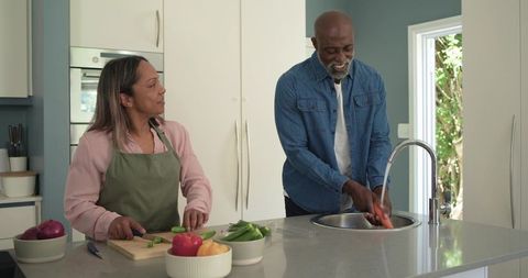 Senior couple preparing healthy meal in modern kitchen washing and chopping vegetables