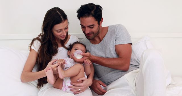 Parents are cuddling with their baby while feeding from a bottle, highlighting family bonding and nurturing. This can be used in advertisements illustrating family life, parenting articles, or promotions of baby products.