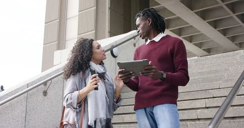 Young diverse coworkers discussing project on tablet on outdoor stairs