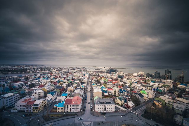 Scenic aerial view of Reykjavik showcases the vibrant, colorful buildings of the Nordic city under a dramatic, cloudy sky. This image captures the urban landscape, giving a sense of the area's characteristic architecture and layout, making it ideal for travel guides, tourism brochures, websites featuring Nordic countries or cityscapes, and blogs discussing urban planning or Icelandic culture.