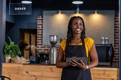 Smiling african american barista holding tablet behind rustic coffeehouse counter