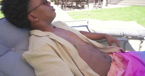 African american man reclining poolside on lounge chair in beige shirt and pink trunks