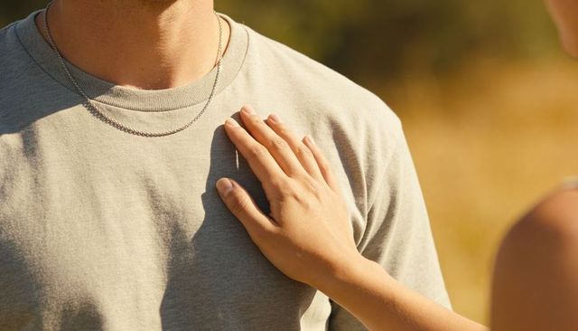 Placing gentle hand on chest of partner wearing silver chains in golden field at sunset