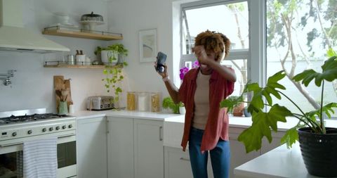 African american woman dancing with smartphone in bright modern kitchen enjoying morning