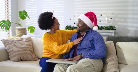 Black couple sharing joyful Christmas moment on couch with Santa hat and cozy decor