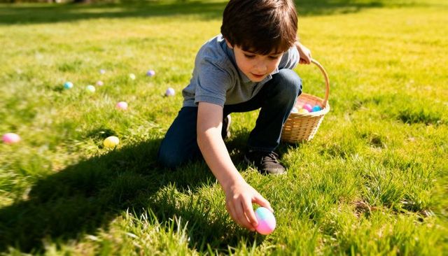 Young boy collecting pastel easter eggs on sunlit lawn with wicker basket, spring outdoor fun