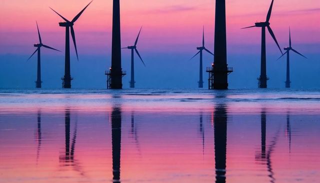 Offshore wind turbines reflecting on calm sea at twilight with pink and blue gradient sky