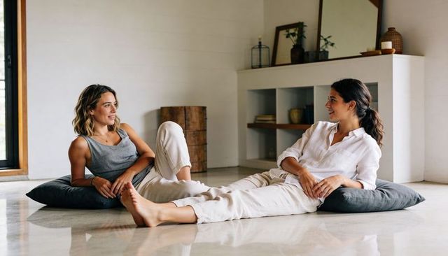 Two women lounging on cushions, relaxing and chatting in minimalist sunlit room