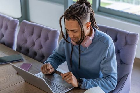 African american man working remotely on laptop with headphones at home office table