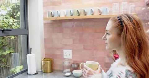 Woman Enjoys Warm Beverage Near Bright Kitchen Window