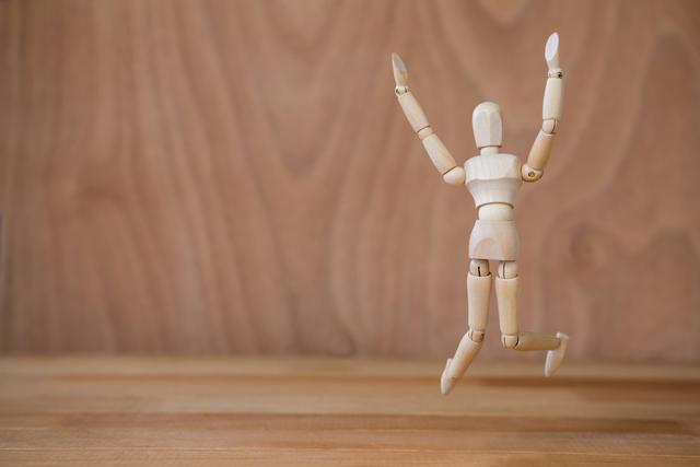 Wooden mannequin jumping on wooden floor, representing creativity, freedom, and joy. Ideal for use in art projects, creative concepts, educational materials, and motivational content.