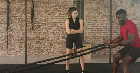 Cross trainer guiding tier workout with battle ropes