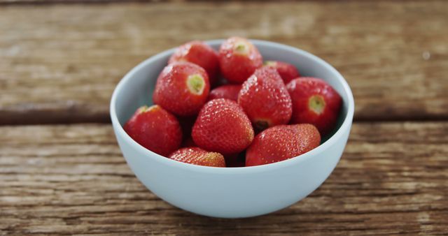 A bowl of fresh strawberries sits on a wooden surface, with copy space. Vibrant and ripe, these berries are a healthy choice for a snack or dessert.