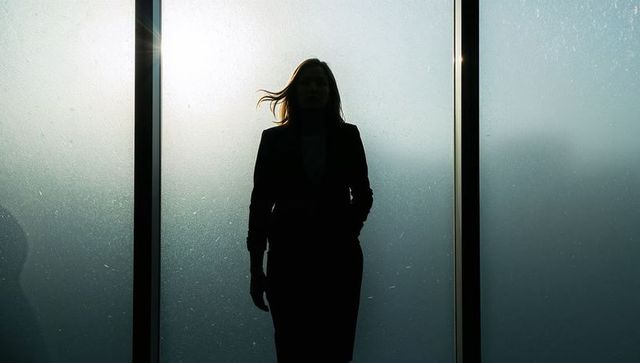 Silhouette businesswoman standing behind frosted glass panels in modern office lobby