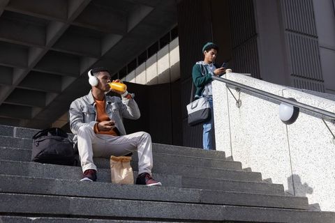 African american students relaxing on campus steps drinking juice listening to music