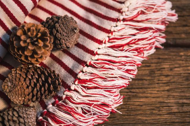 This image captures a close-up view of pine cones placed on a striped blanket with a wooden table background. Ideal for use in autumn-themed projects, home decor inspiration, or promoting cozy and rustic settings. Perfect for blogs, social media posts, or advertisements related to seasonal decor and nature.