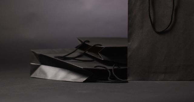 Sophisticated black shopping bags lying on a dark surface for a sleek and modern presentation. Ideal for use in retail advertising, promotional materials for luxury brands, packaging design showcases, and minimalist-themed marketing campaigns.