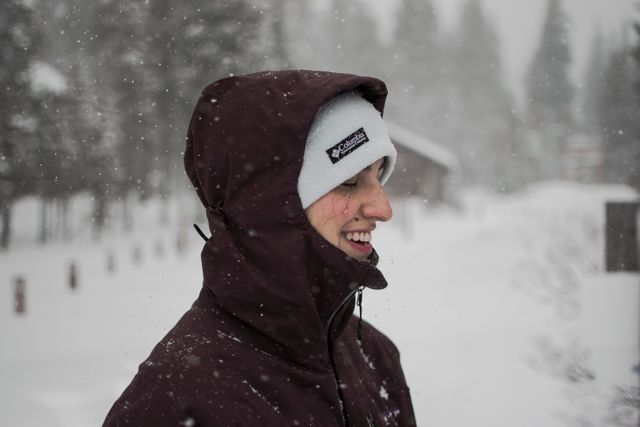 Person wearing jacket and beanie smiling while enjoying snowfall. Perfect for depicting winter activities, cold weather attire, and outdoor enjoyment in a snowy environment.