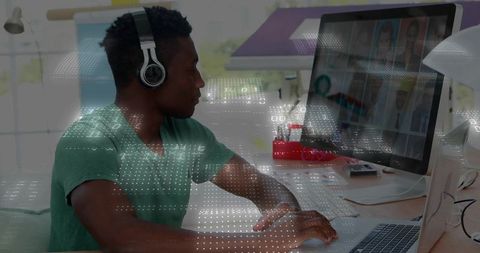 Designer typing at desktop with headphones, laptop, color swatches and digital data overlays