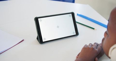 African male teen wearing headphones watching tablet for remote learning and focused study