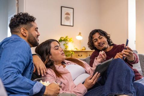 Friends sharing popcorn and streaming on tablet and phone during cozy at-home movie night
