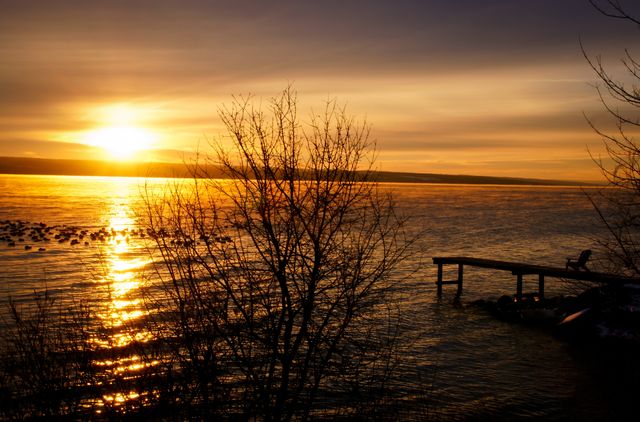 Serene Lakeside Sunrise with Golden Glow and Silhouette Pier - Download Free Stock Photos Pikwizard.com