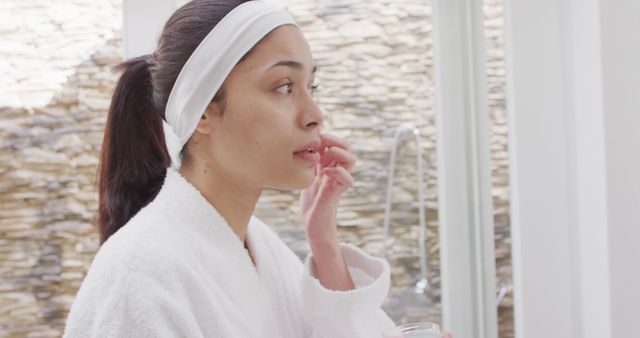 Biracial woman applying cream on face in bathroom. Beauty, health and female spa home concept.