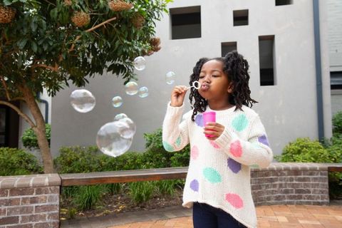 Child blowing soap bubbles in courtyard on a sunny day