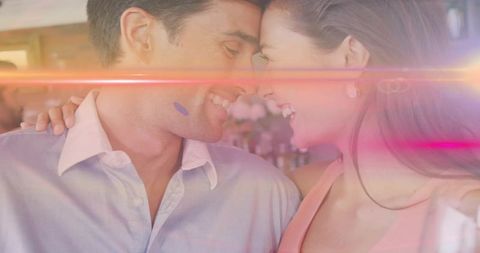 Romantic couple leaning foreheads and smiling in bar with warm lens flare and soft bokeh
