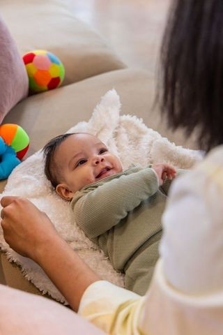 Smiling infant bonding with caregiver on cozy sofa with soft blanket and colorful toys