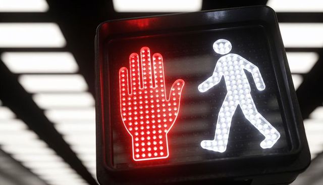 Pedestrian signal showing red hand and white walking figure under canopy lights, closeup
