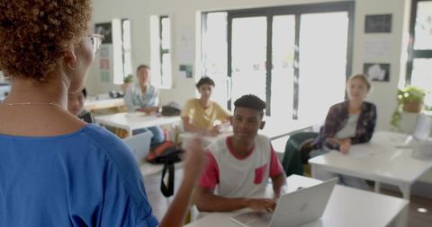 Teacher leading interactive classroom discussion with students and laptop in sunlit room