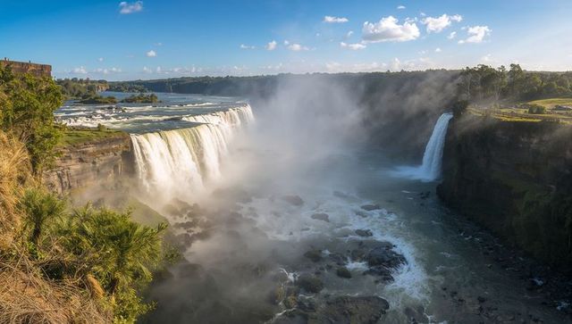 Panoramic waterfall cascade sending thick mist across river gorge with grassy overlook