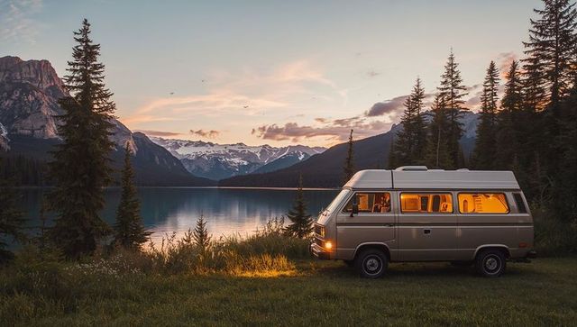 Retro camper van at lakeside golden hour with warm interior glow and mountain reflection