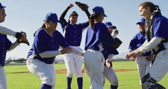 This depicts a group of young girls in blue baseball uniforms celebrating enthusiastically on an outdoor field. Suitable for use in articles or campaigns covering youth sports, team building, gender equality in sports, and highlighting the joy of athletic accomplishments.