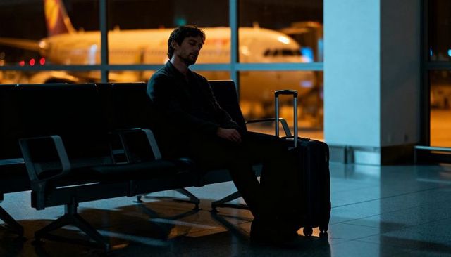Solitary traveler resting at airport gate late night with suitcase and airplane window