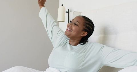 African american woman in her 30s stretching in bed wearing mint loungewear morning calm
