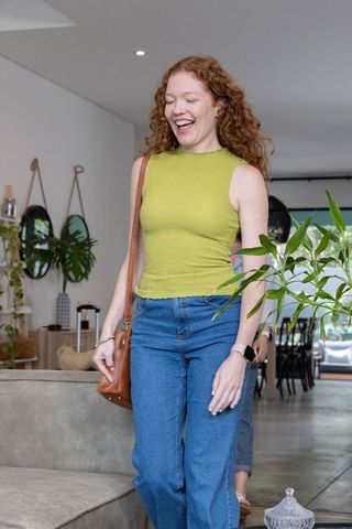 Curly redhead woman walking through bright modern home with plants wearing lime green top