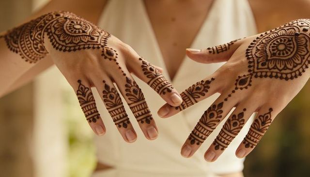Woman showing intricate mehndi henna designs on hands and forearms in white halter
