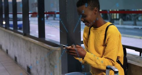 Woman in yellow sweater using smartphone at bus stop with suitcase and backpack