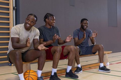 African american basketball teammates cheering and clapping on bench in indoor gym