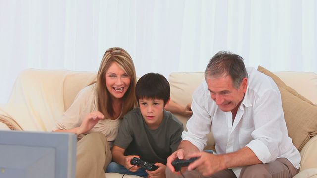 Grandparents engaging in a fun moment with their grandson while playing video games in the living room. Great for illustrating family bonding, intergenerational activities, and home leisure. Useful for advertisements, blogs about family life, and social media posts emphasizing happy family moments.