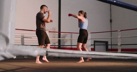 Female boxer sparring with coach in boxing ring during focused training session
