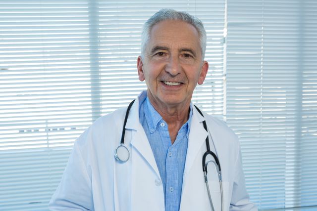 Senior doctor smiling in clinic, wearing white coat and stethoscope. Ideal for healthcare advertisements, medical websites, patient care brochures, and health service promotions.