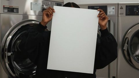Anonymous person holding blank poster in modern laundromat